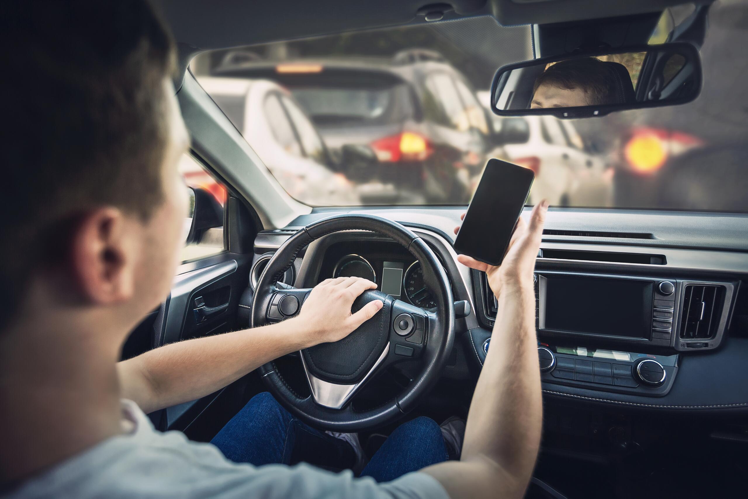 Driver holding smartphone in traffic represented by Fort Worth Uber accident lawyers.