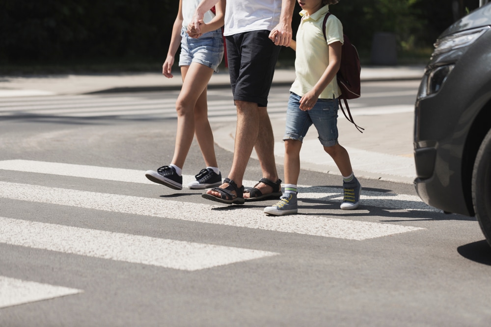Dallas pedestrian accident lawyer crossing street with family in crosswalk near approaching vehicle.