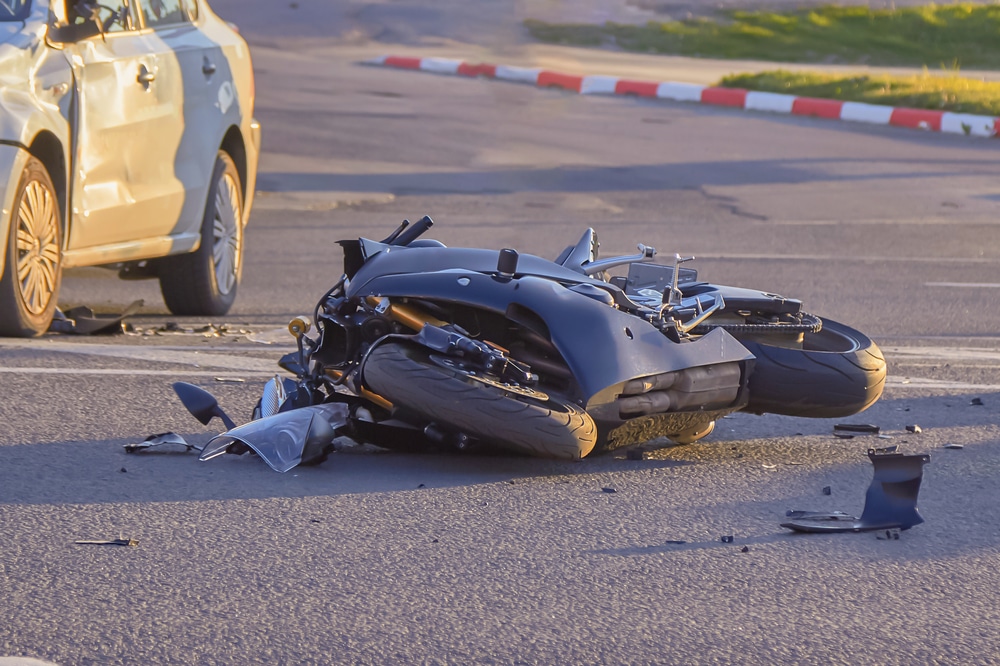 Dallas motorcycle accident lawyer showing crashed motorcycle on roadway after collision with damaged vehicle nearby.