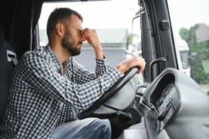 Fatigued truck driver holding head while driving, situation a Dallas truck accident lawyer may investigate