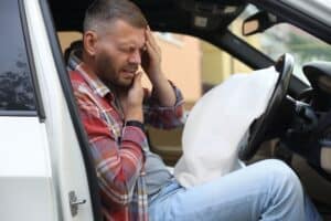 Injured driver holding head after crash with deployed airbag, situation a Dallas car accident lawyer may help investigate.